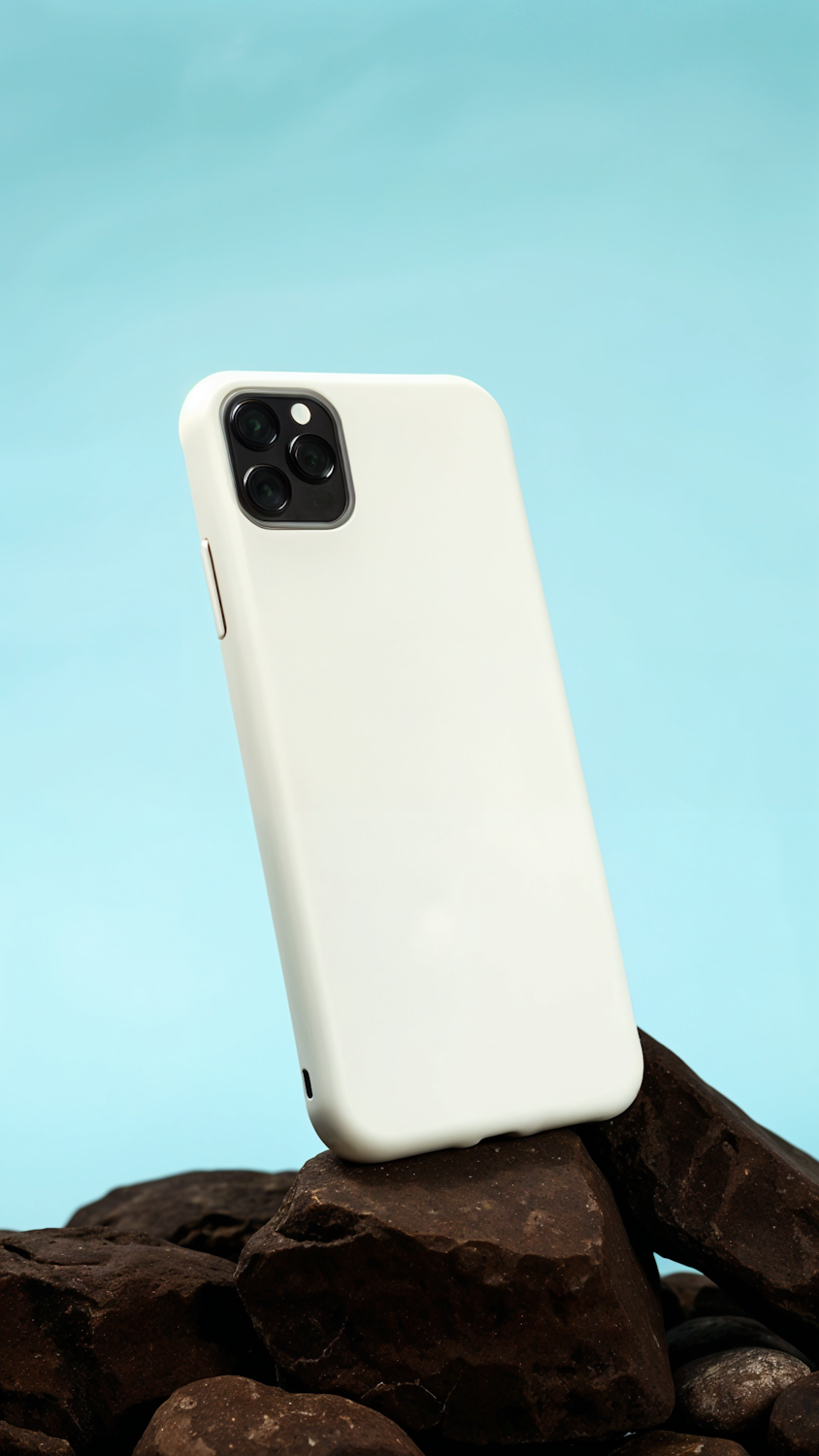 Smartphone in a matte white case resting on dark rocks