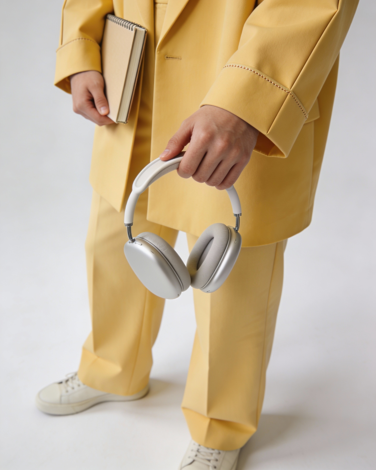 Person in a yellow suit holding silver over-ear headphones
